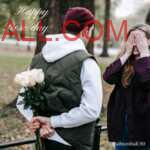 red cap and hood jacket wearing man with pink rose bouquet hiding at back and girlfriend closing with hands and smiling & waiting for surprise