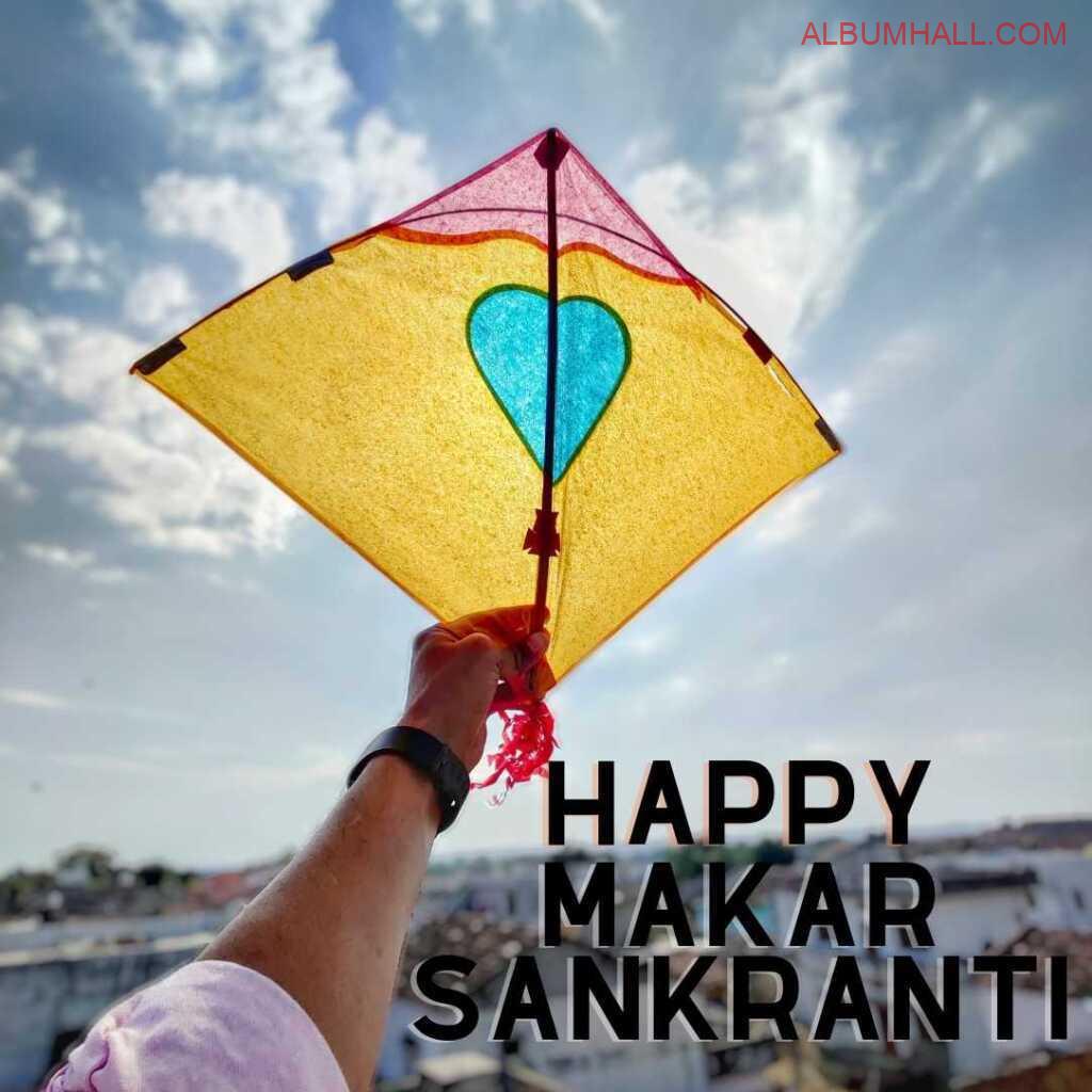 Person holding yellow kite with blue color heart in the center to celebrate Makar sakranti