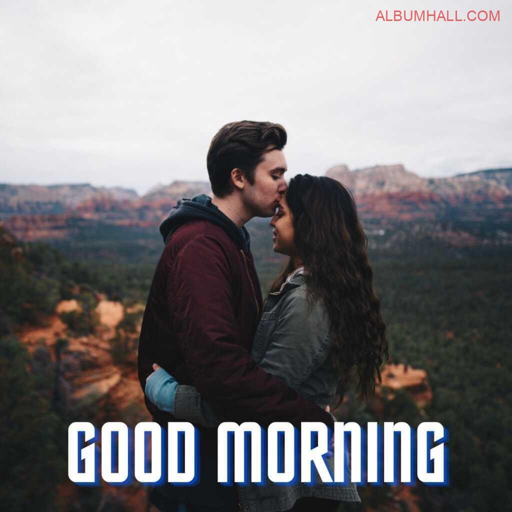 a boy wearing jacket kissing his a girl on her forehead early morning on a hill top